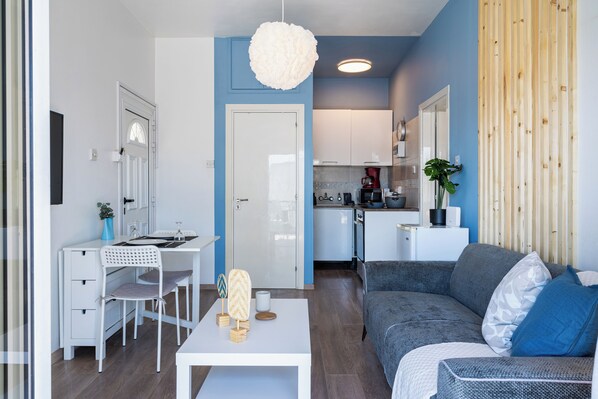 A modern living room with a white desk, a grey sofa, and a hanging light fixture.