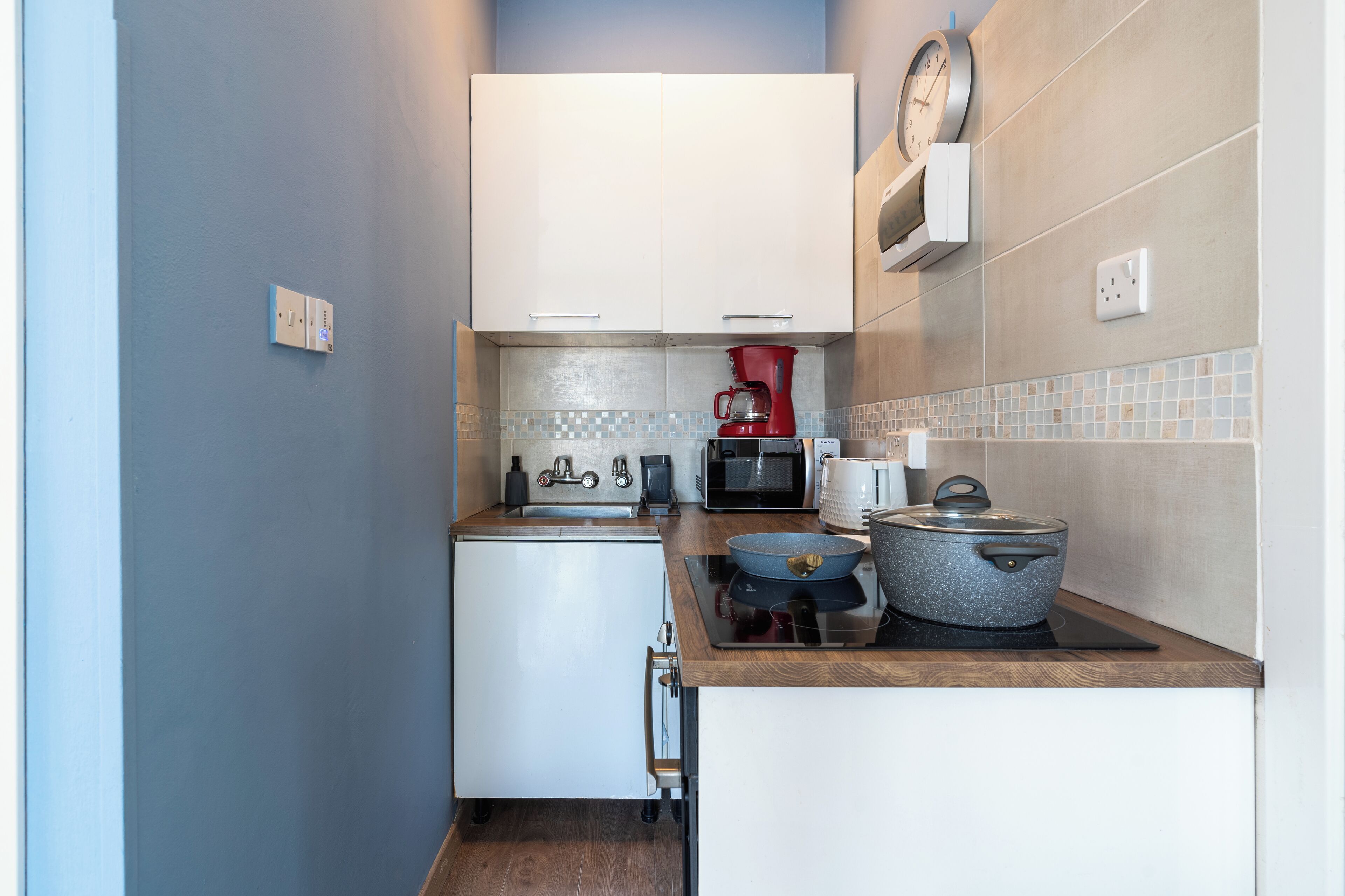A compact kitchen with white cabinets, a microwave, a coffee maker, and a stove.