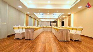A conference room with a long table, white chairs with gold sashes, wooden flooring, and recessed ceiling lighting. - AYANSH KLYDE INN (Lucknow)