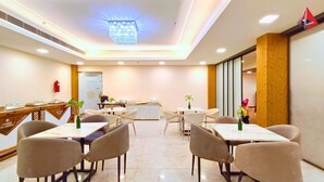 A hotel dining area with multiple tables and chairs, a chandelier, and a fire extinguisher on the wall. - AYANSH KLYDE INN (Lucknow)