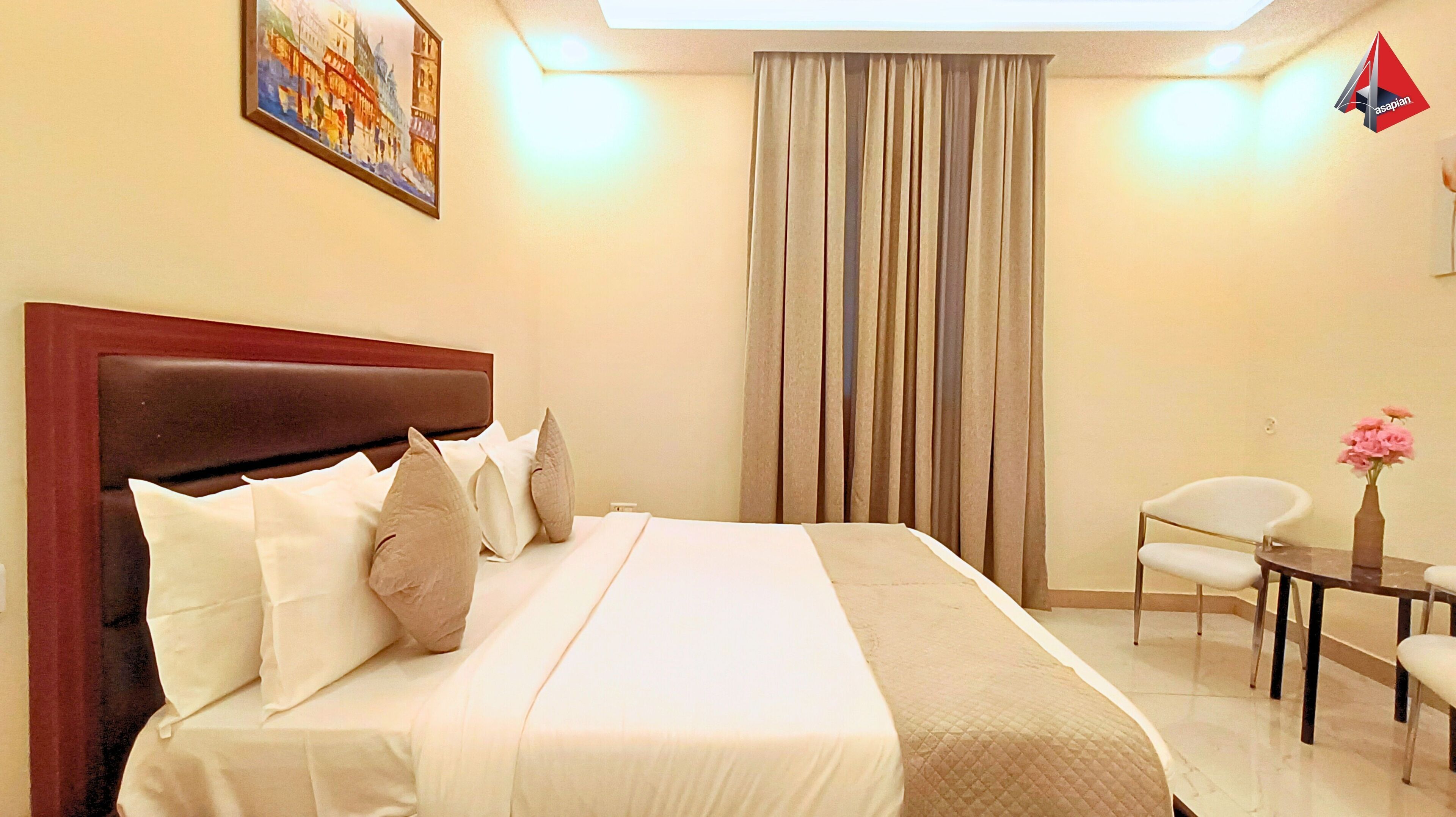 A hotel room with a large bed, a headboard, a desk with a chair, a vase with flowers, and a painting on the wall.