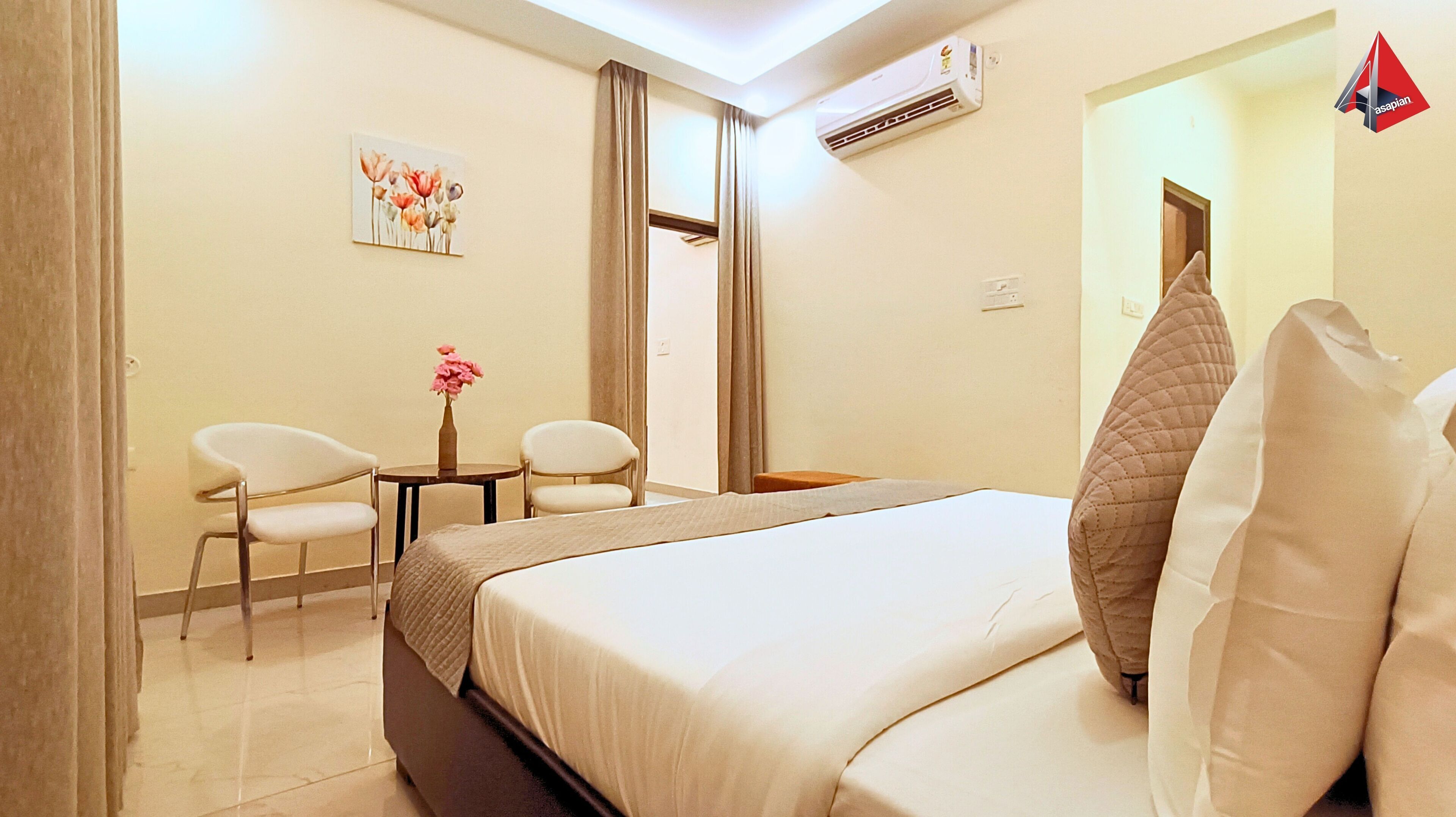 A hotel room with a bed, two chairs, a small table with a vase, an air conditioner, and a painting on the wall.