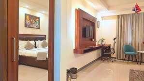 A hotel room with a bed, a desk, a chair, a TV, and a window with curtains. - AYANSH KLYDE INN (Lucknow)