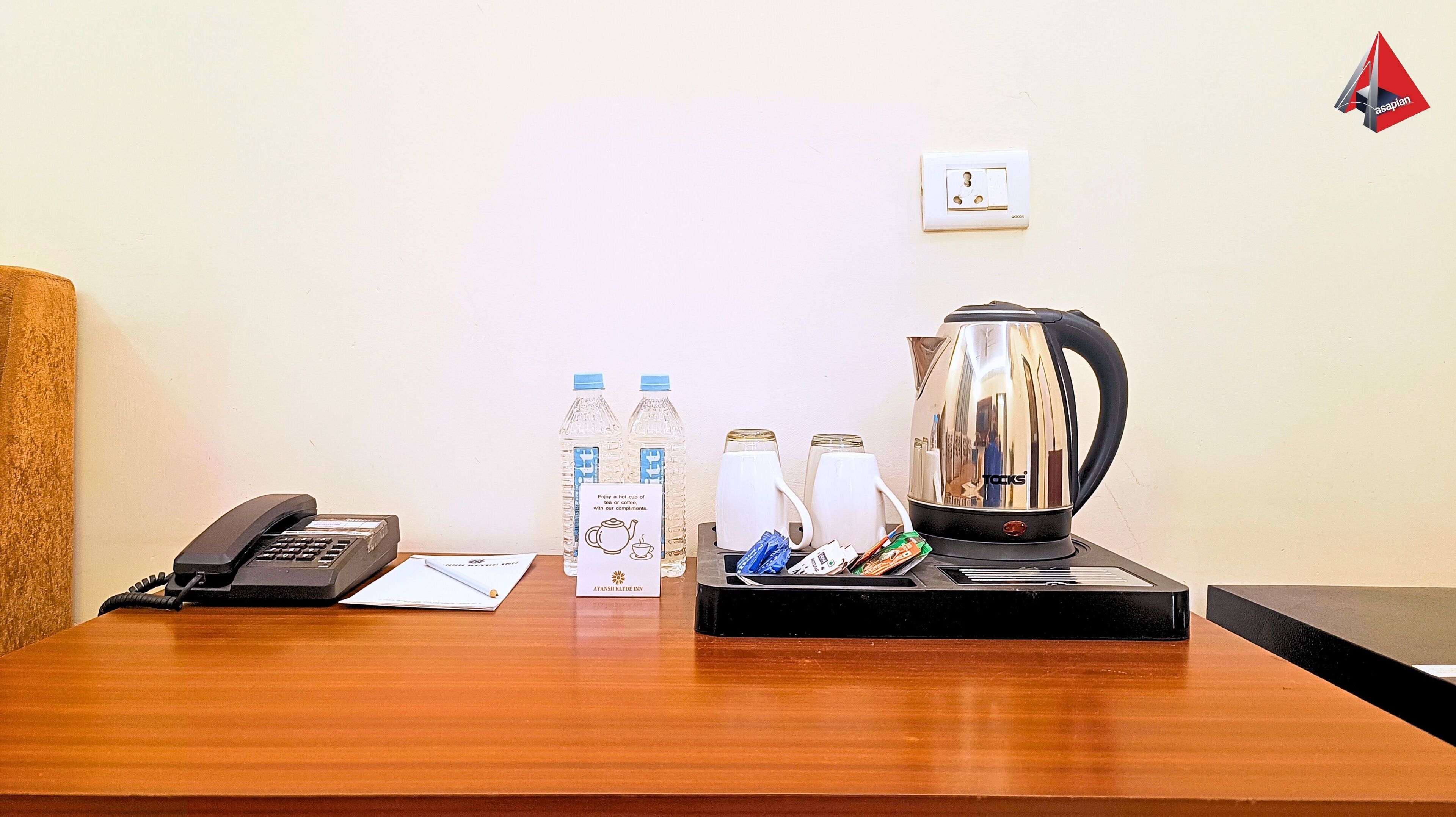 A hotel room with a wooden desk, a telephone, a kettle, bottled water, and a coffee maker.