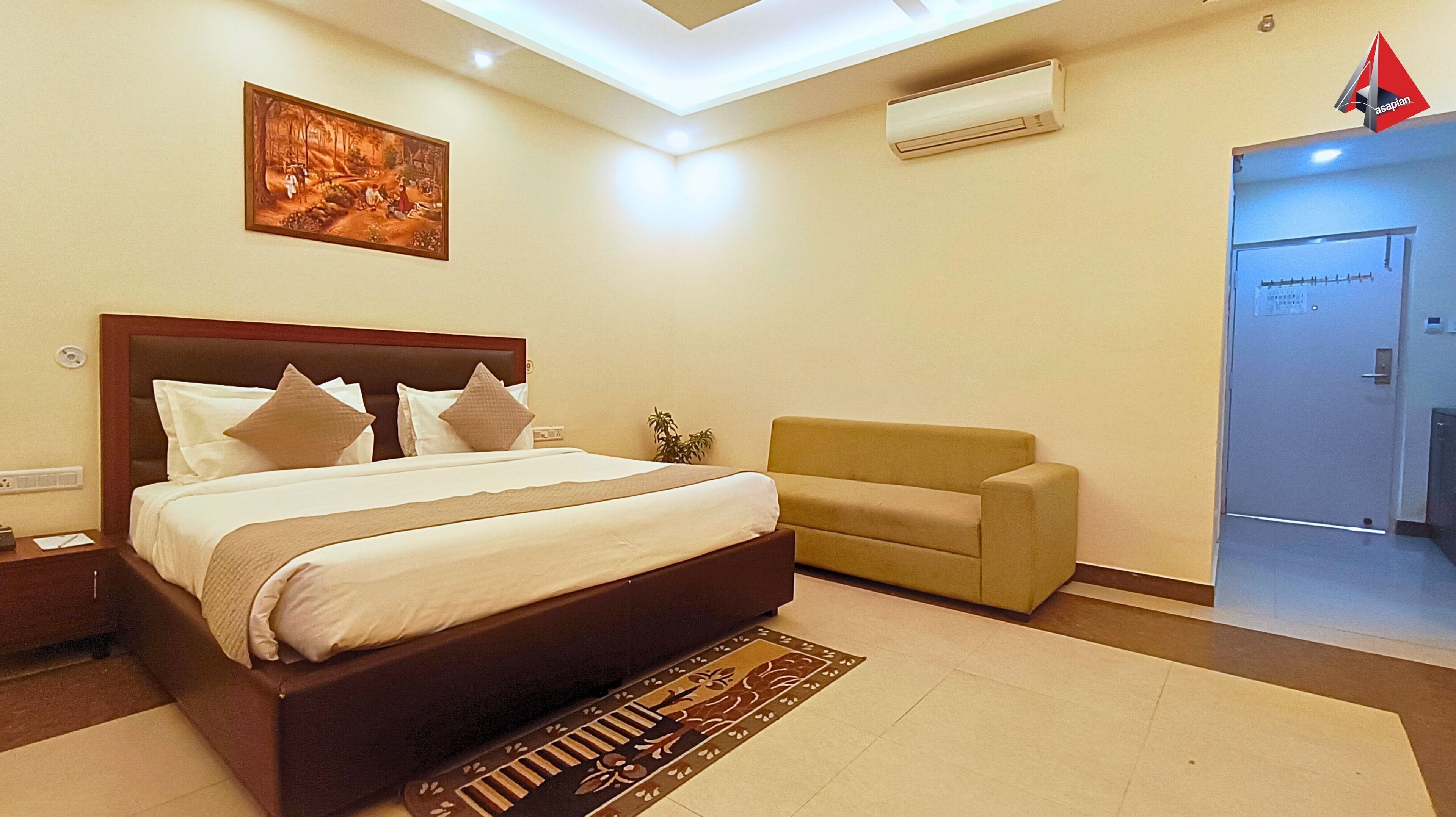 A hotel room with a bed, a sofa, a painting on the wall, an air conditioning unit, and a door with a sign.