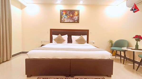 A hotel room with a large bed, a small table with a vase, and a painting on the wall. - AYANSH KLYDE INN (Lucknow)