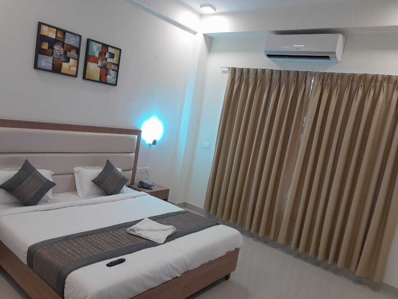 A hotel room with a large bed, a bedside table, an air conditioner, and curtains.