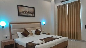 A neatly made bed with a headboard, two bedside tables, a wall-mounted painting, and a large window with curtains. - Hotel The Luxem (Gurugram)