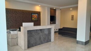 A reception area with a marble counter, a sofa, and a TV mounted on the wall. - Hotel The Luxem (Gurugram)
