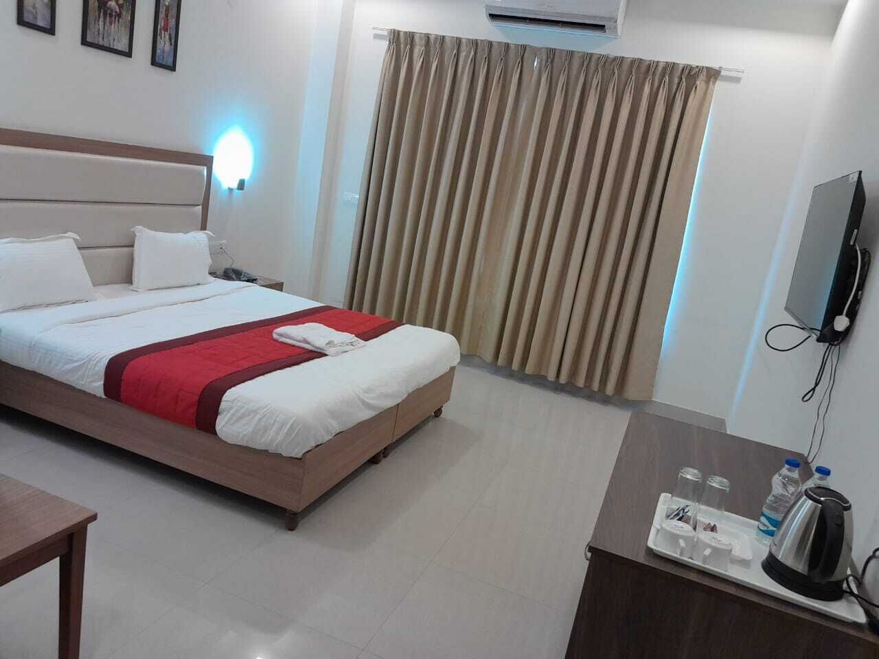 A hotel room with a bed, bedside table, and a desk with a kettle and water bottle.