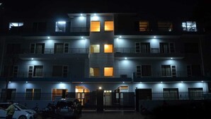 A multi-story building with illuminated windows and a gated entrance. - Hotel The Luxem (Gurugram)