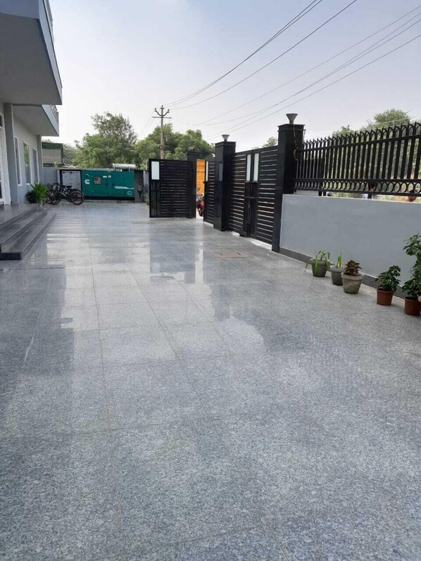 A paved walkway leading to a gated entrance with a metal fence and potted plants. - Hotel The Luxem (Gurugram)