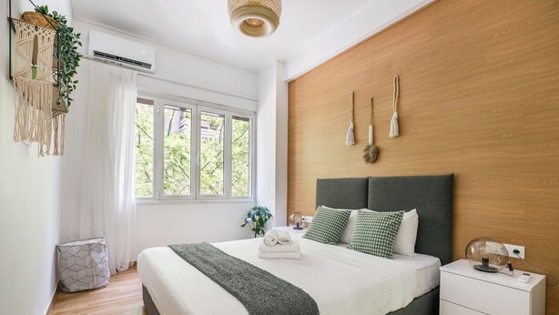 Une chambre moderne avec un grand lit, des tables de chevet, un mur décoratif en bois et une fenêtre avec des rideaux.