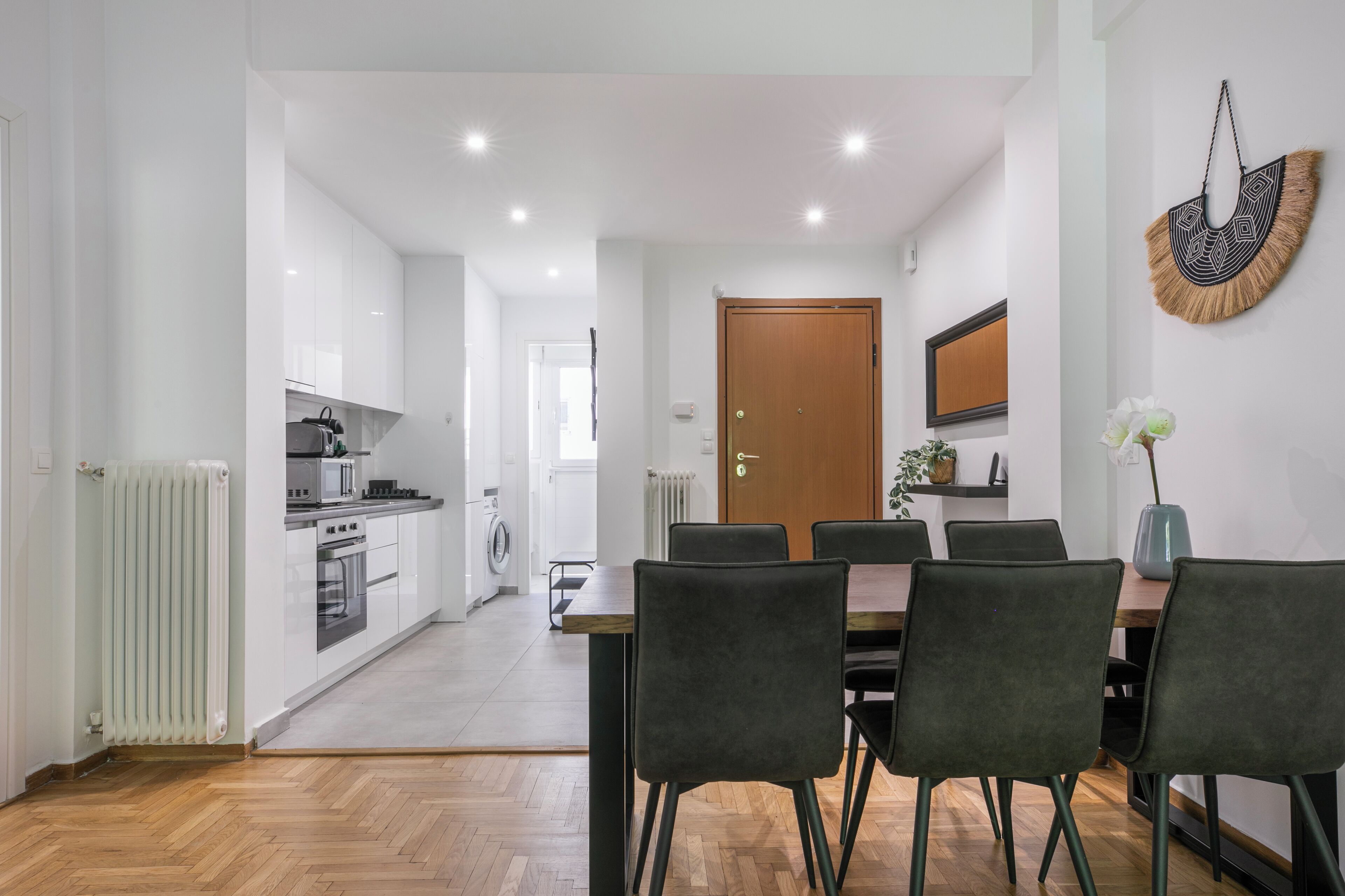 A modern kitchen with white cabinets and a dining area with a wooden table and black chairs.