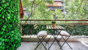 Un balcon avec une table en bois et deux chaises, entouré d’un luxuriant feuillage verdoyant.