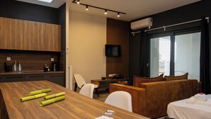 A modern hotel room with a wooden dining table, a sofa, a bed, and a TV mounted on the wall. - Dioroh Suites Meteora 304 (Kalampaka)