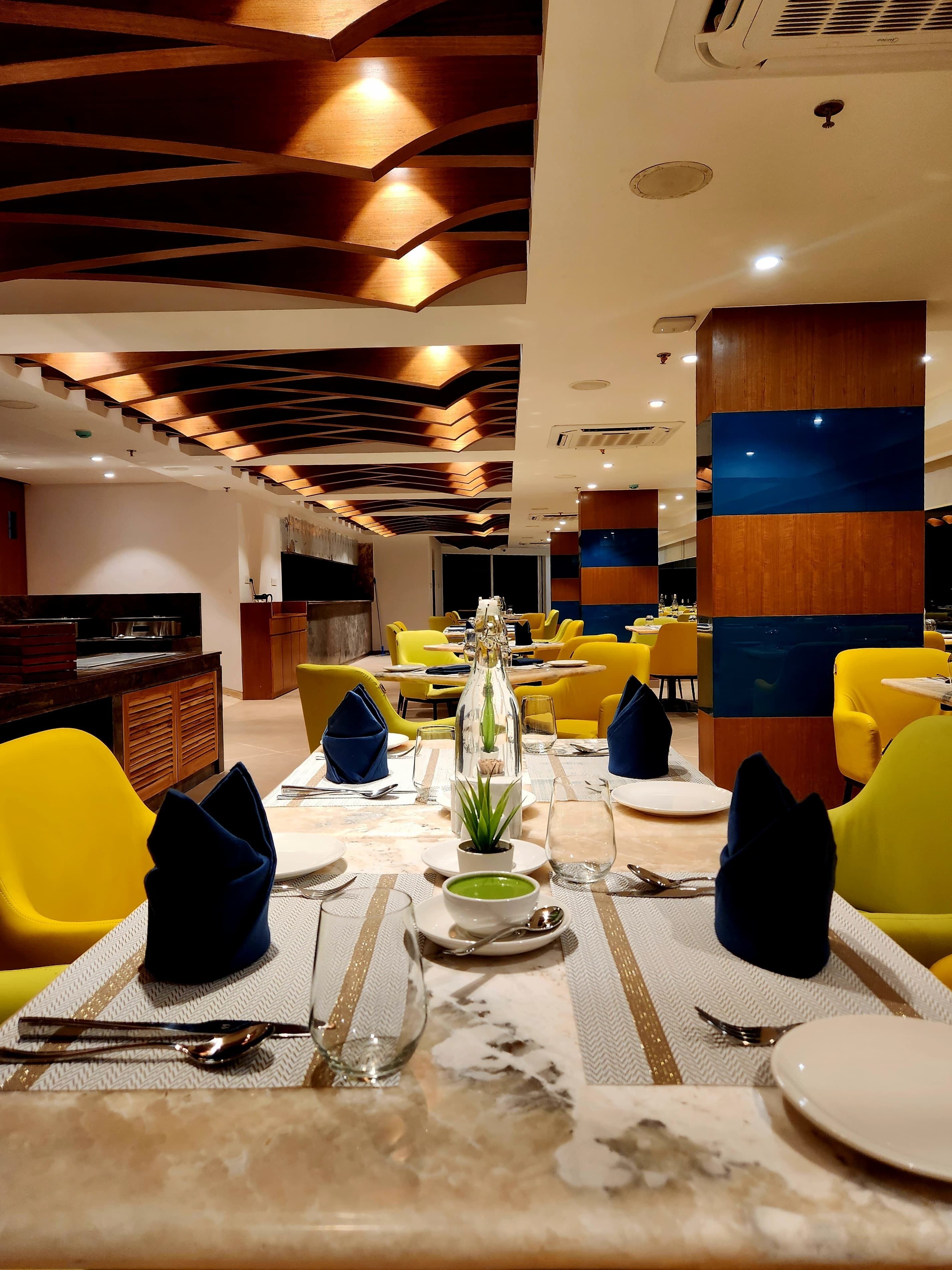 A restaurant with yellow chairs, a marble table, and a modern ceiling design.