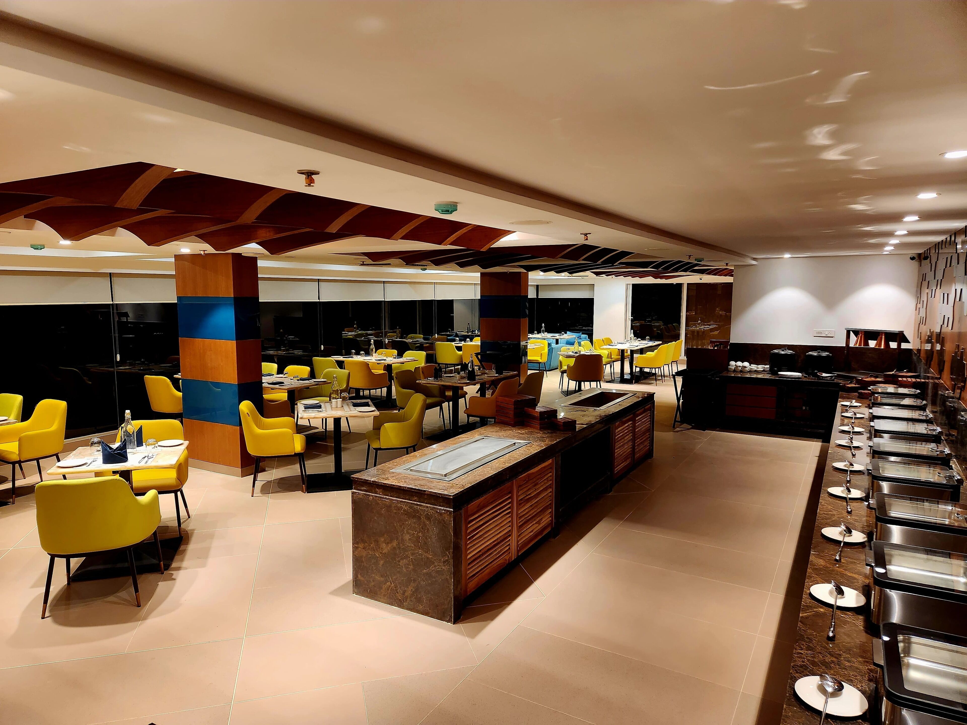 Un restaurante moderno con sillas amarillas, una zona de buffet central y una barra.