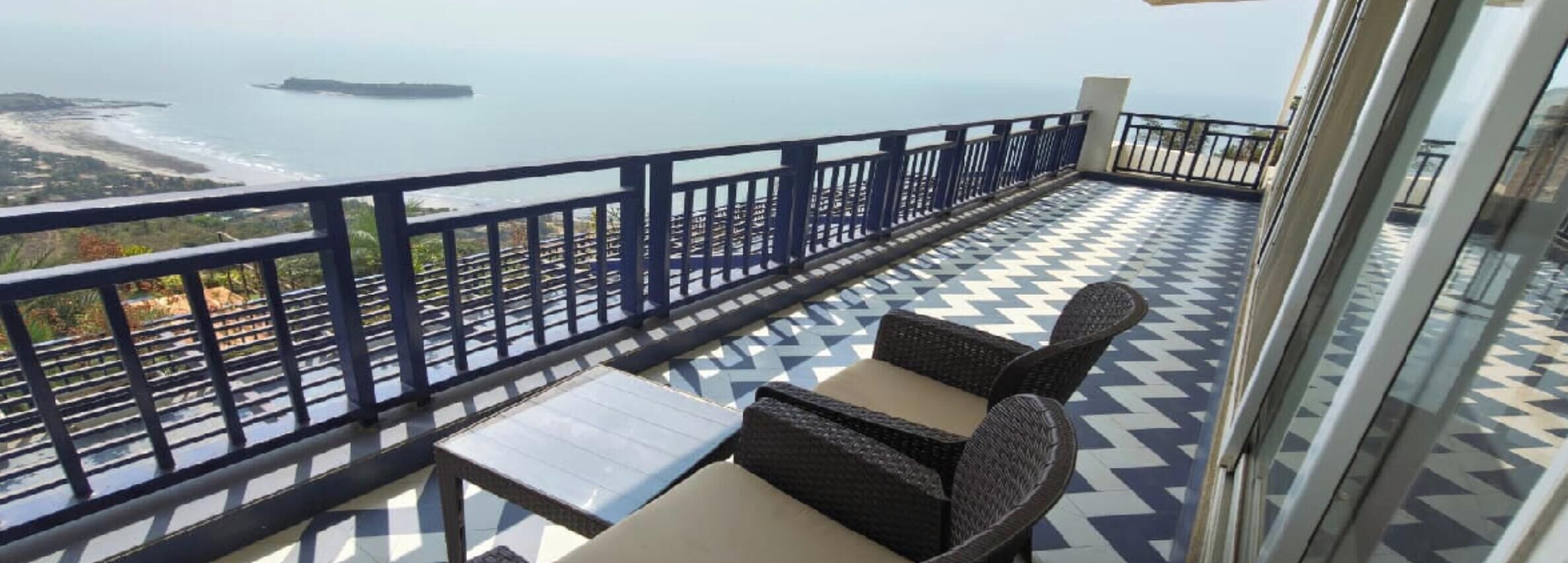 Un balcón con vista al mar, suelo estampado y muebles de mimbre.
