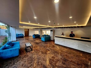 A modern lobby with a marble floor, blue sofas, and a reception desk.