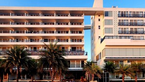 Un hotel de varios pisos con balcones, palmeras y cielo despejado.