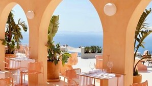 An outdoor dining area with tables and chairs, potted plants, and a view of the sea. - Hotiday Mykonos Fanari (Mykonos)
