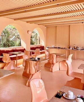 Un comedor moderno con sillas originales, una mesa larga y vistas a la vegetación a través de ventanas de arco.