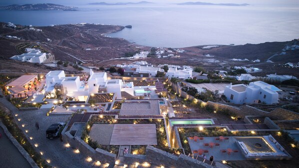 Vista aérea de un pueblo costero con edificios blancos, una piscina y una carretera que conduce al mar.