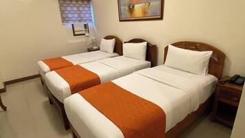 A hotel room with two beds, a painting on the wall, a window with blinds, and a bedside table with a phone.