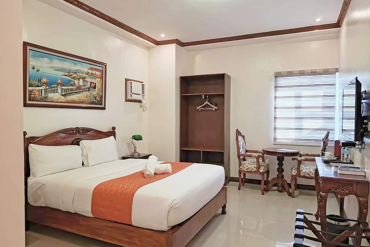 A hotel room with a large bed, a desk with a chair, a coat rack, and a painting on the wall.