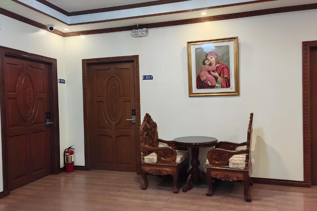 Un hall de hotel con dos puertas de madera, un cuadro enmarco, una mesita redonda y dos sillas decorativas.
