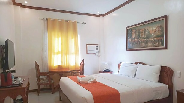 A hotel room with a large bed, a desk with a television, a dining table, and a painting on the wall. - Ferrymar Hotel Iloilo (Iloilo)