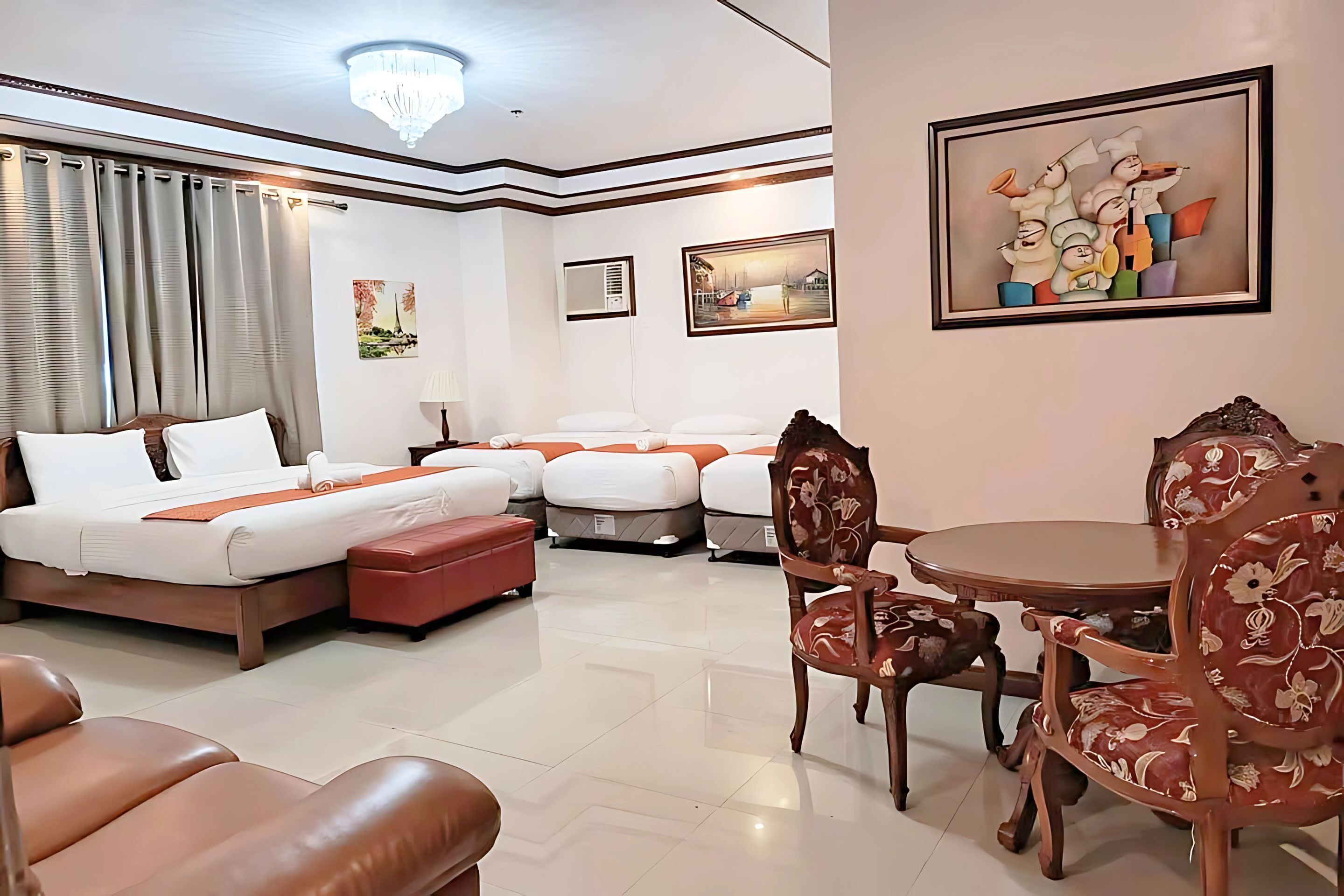 A hotel room with a large bed, two smaller beds, a dining table with chairs, and artwork on the walls.