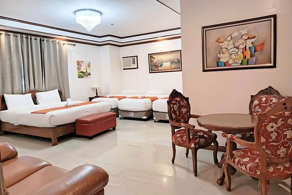 A hotel room with a large bed, two smaller beds, a dining table with chairs, and artwork on the walls.