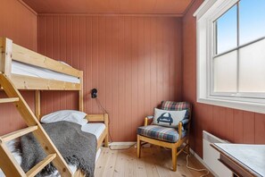 A room with a bunk bed, a chair with a plaid cushion, and a window.
