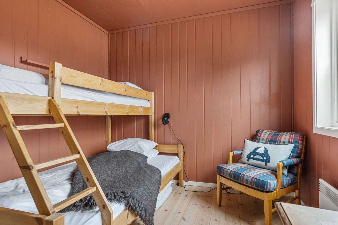 Una cama litera con escalera, una silla con cojín escocés y un radiador en la pared.