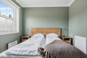 A bedroom with a wooden headboard, two bedside tables, a radiator, and a window.