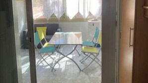 A room with a sliding glass door leading to an outdoor patio area. Inside, there is a table with chairs, a sofa, and a small cabinet. - Studio 1 to 4 persons (Bandol)