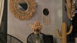 A room with a round woven mirror, a small round mirror, and a cactus decoration. There is a chair and a table with a vase of dried flowers. - Rental house with pool and Jacuzzi (Restinclières)