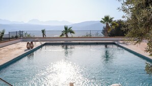 A rectangular swimming pool with a tiled deck, a metal fence, and a view of distant mountains.