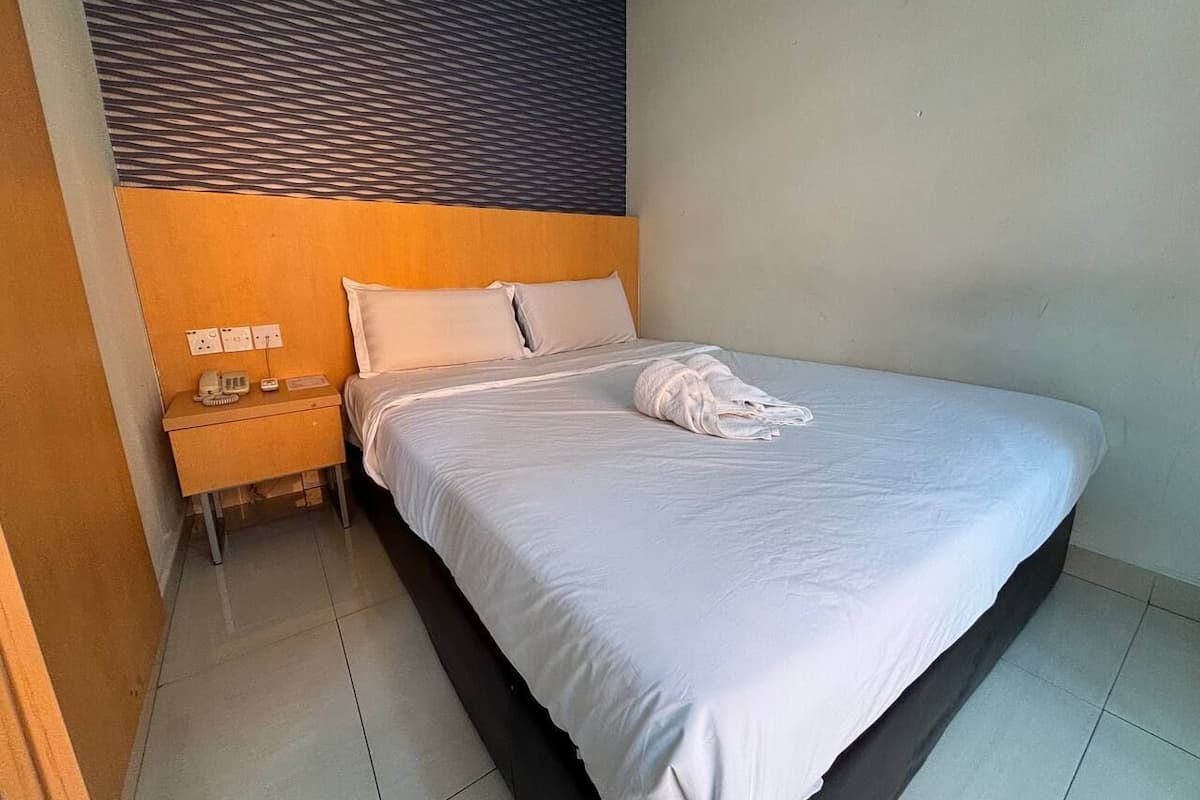 Quarto de hotel com cama, mesa de cabeceira e painel fixado na parede.