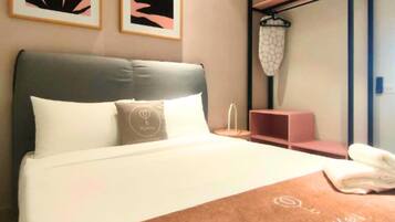 Una habitación de hotel con una cama, una mesita de noche, un estante con una cesta colgante y dos cuadros abstractos enmarcados en la pared.