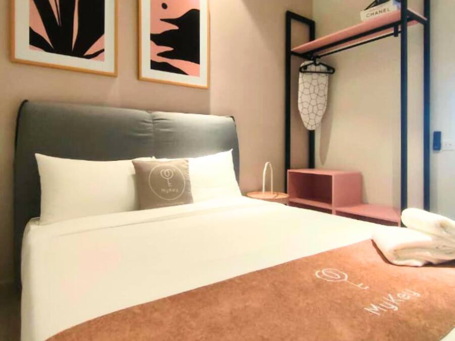 Una habitación de hotel con una cama, una mesita de noche, un estante con una cesta colgante y dos cuadros abstractos enmarcados en la pared.