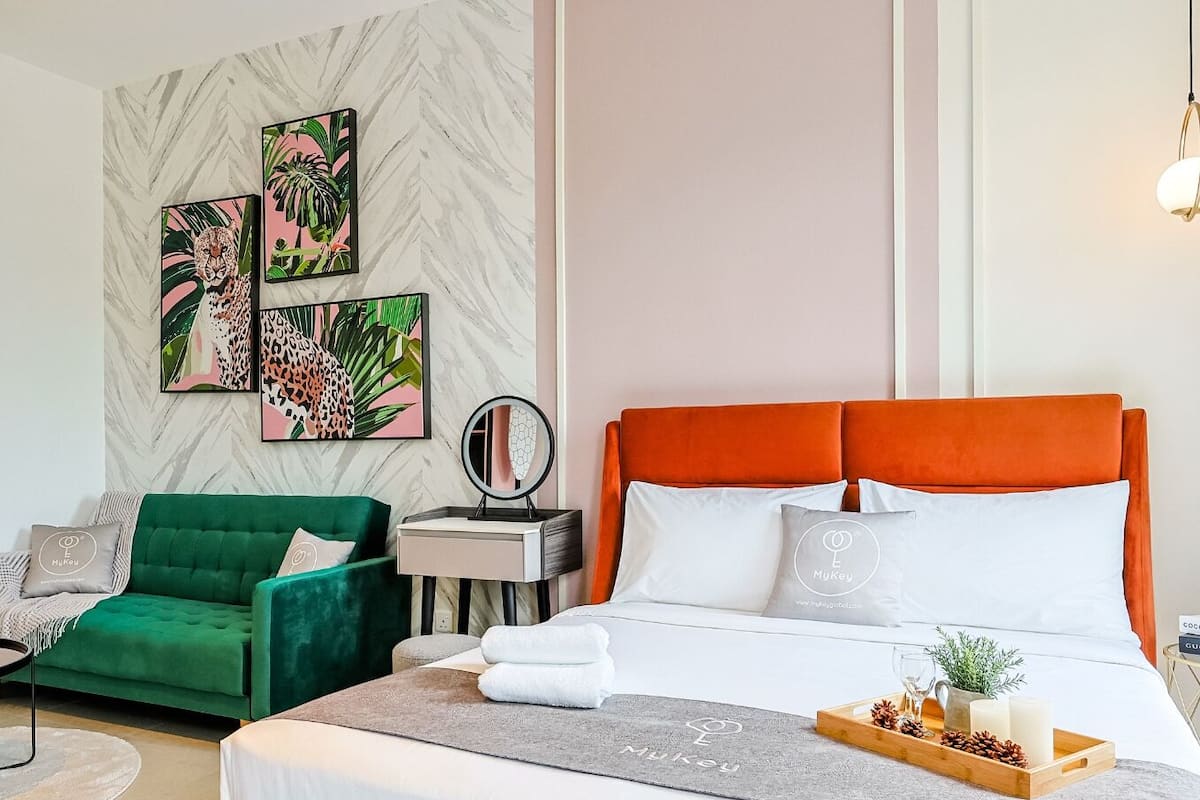 A hotel room with a large bed, green armchair, and two wall art pieces.