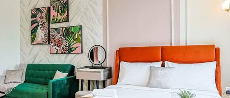 A hotel room with a large bed, green armchair, and two wall art pieces.