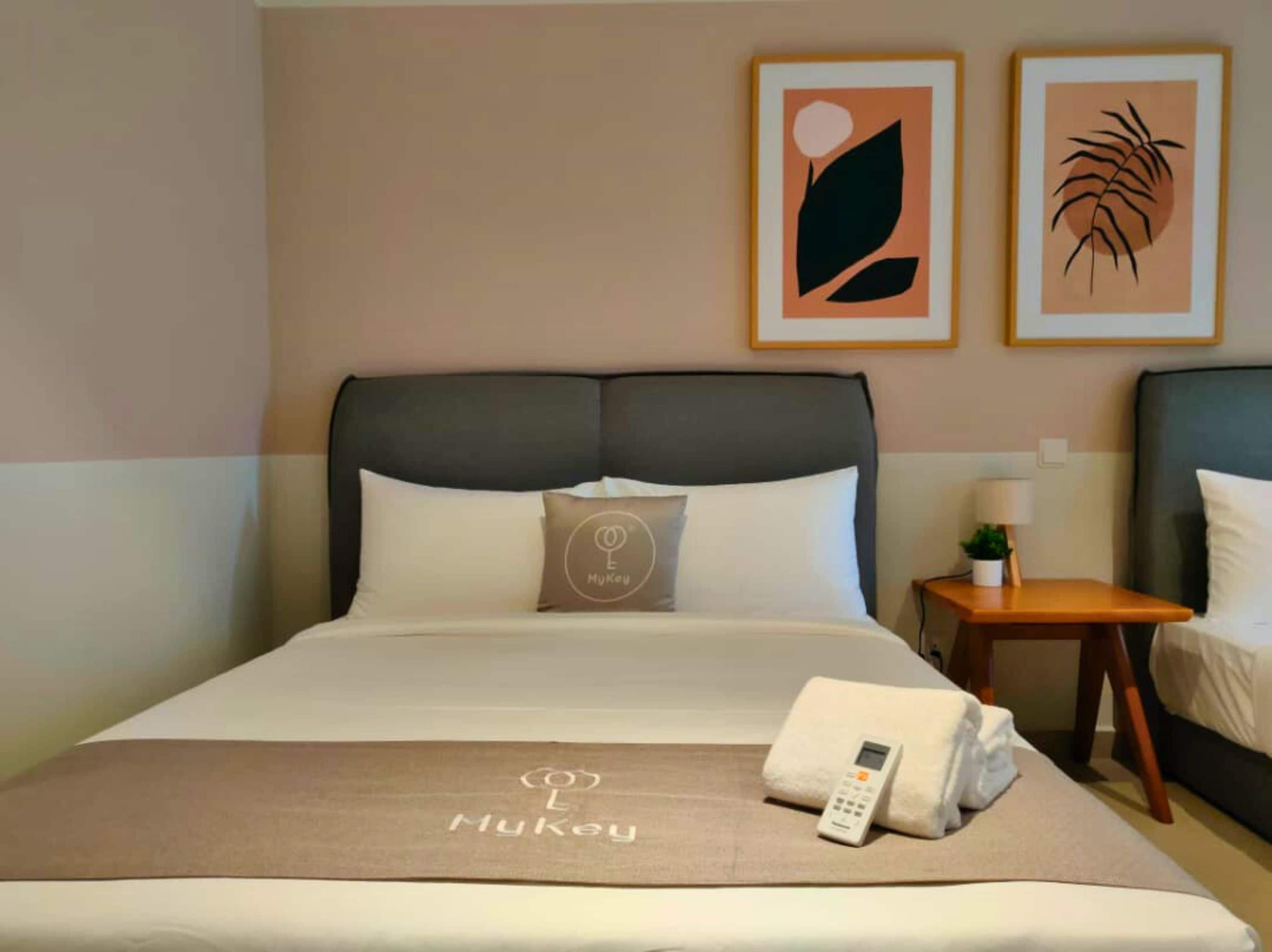 A hotel room with a bed, a bedside table with a lamp, and two framed wall art pieces.