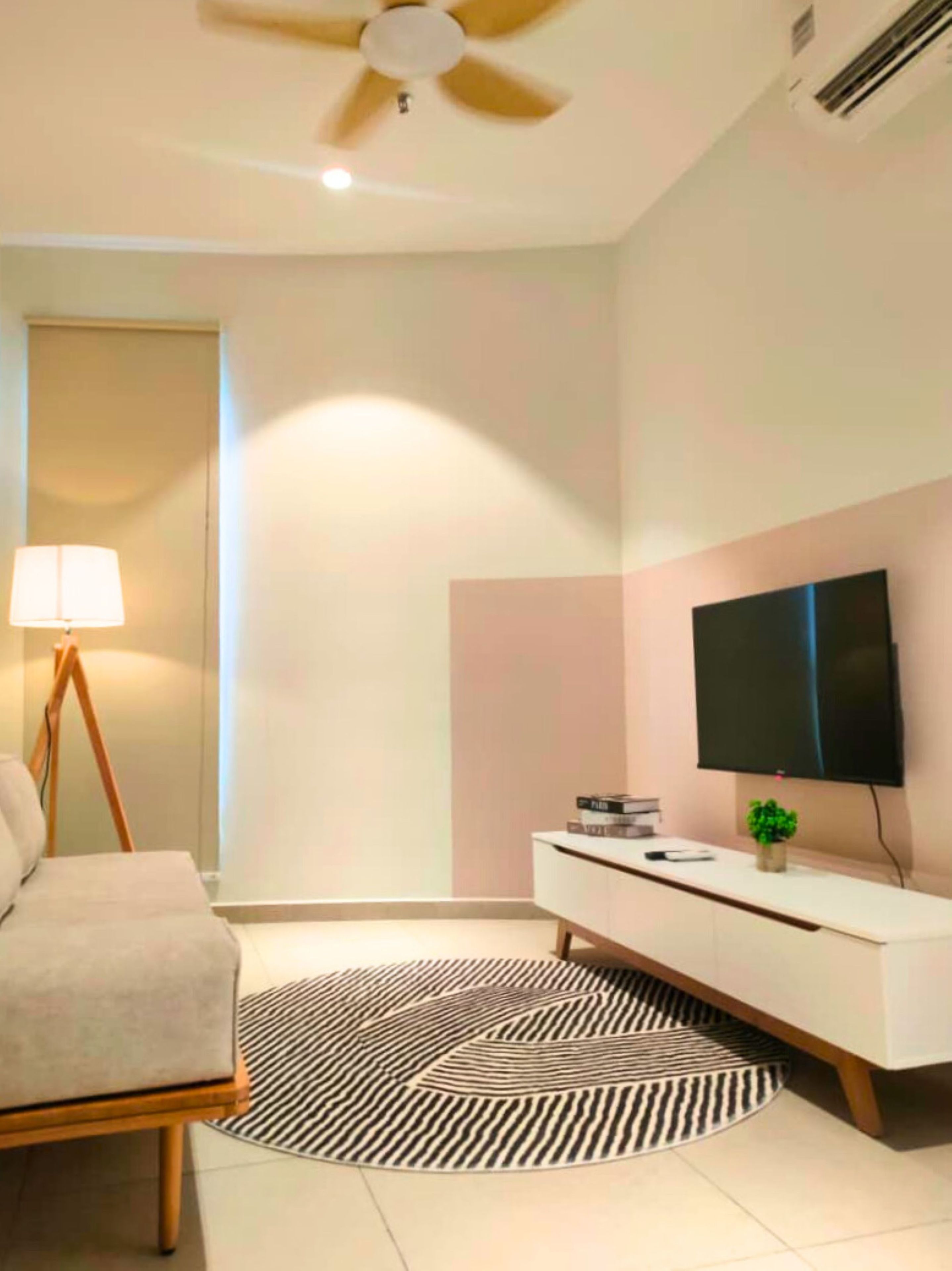 Un dormitorio moderno con una cama, una lámpara de noche, un televisor en la pared y una planta pequeña en la mesita de noche.