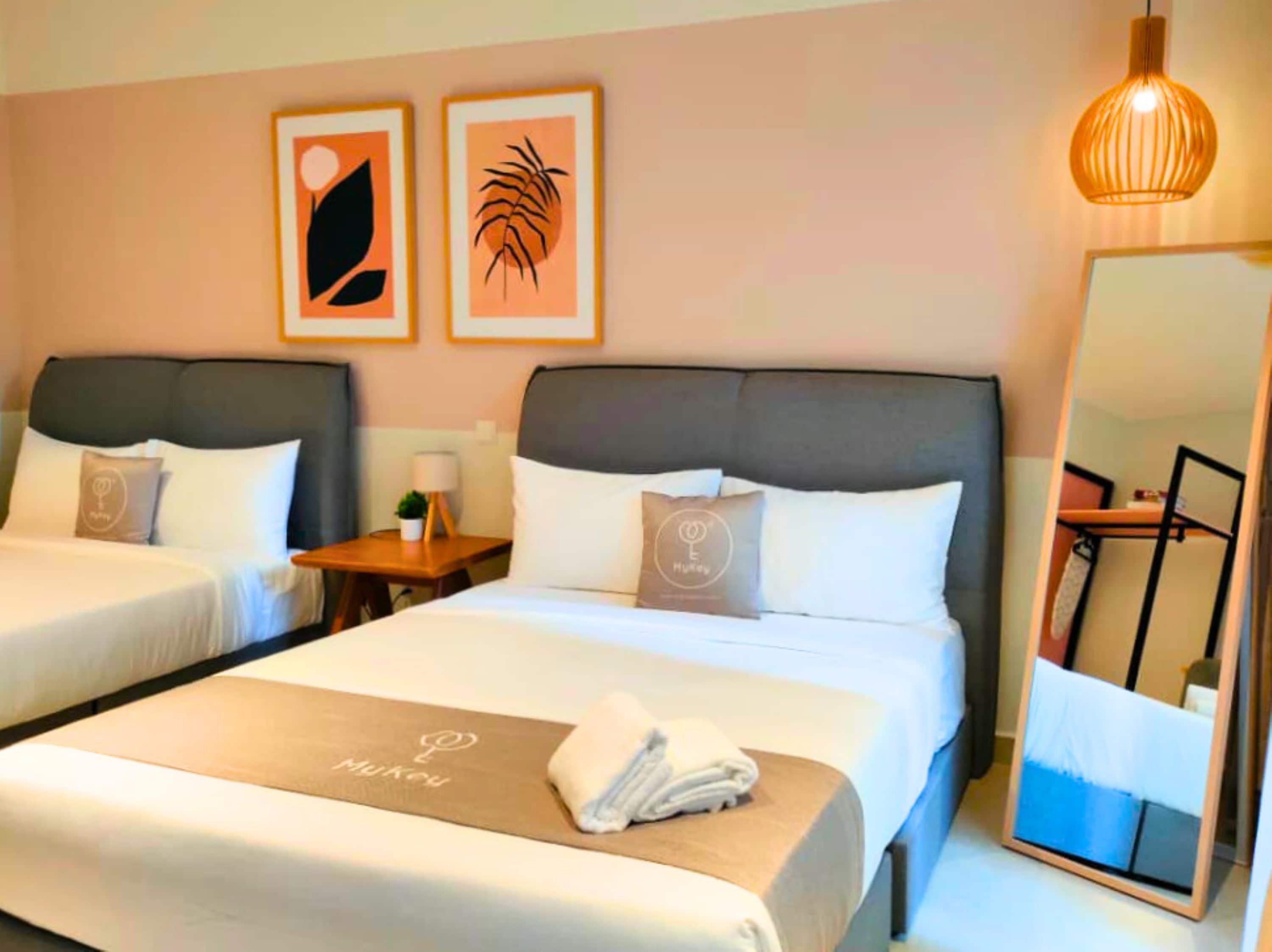 A hotel room with two beds, a bedside table with a lamp, a mirror, and artwork on the wall.