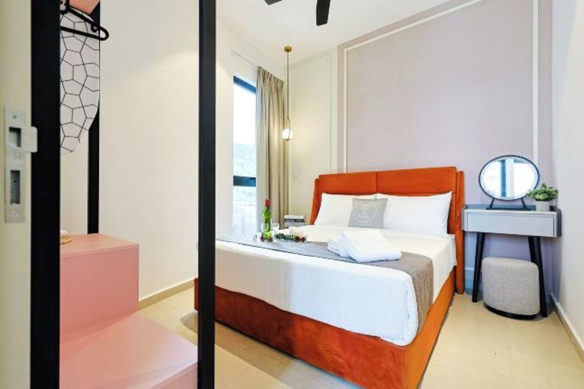 A hotel room with a bed, a bedside table, a mirror, and a small stool.