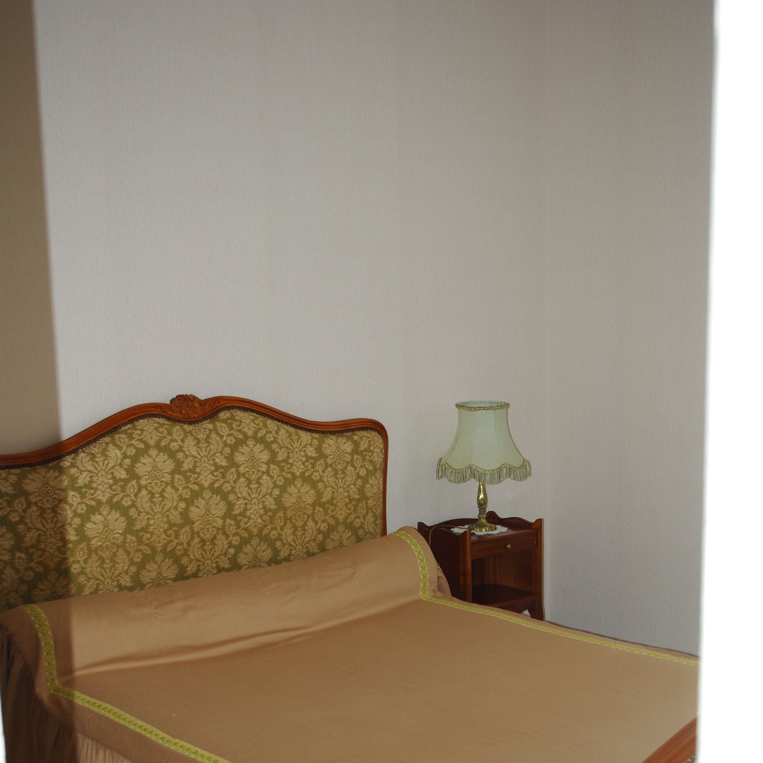 A bed with a floral headboard and a green lampshade on a bedside table.